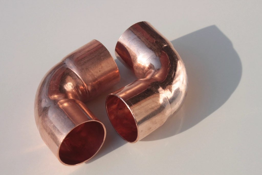 Two copper elbow pipe fittings on a white surface
